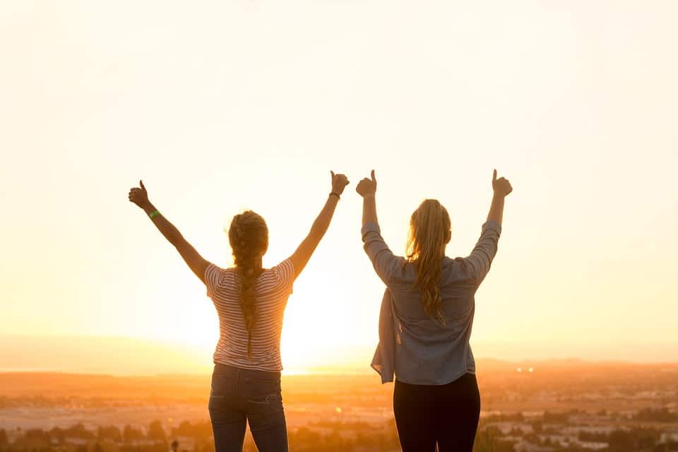 Twee dames bij zonsondergang met duim omhoog